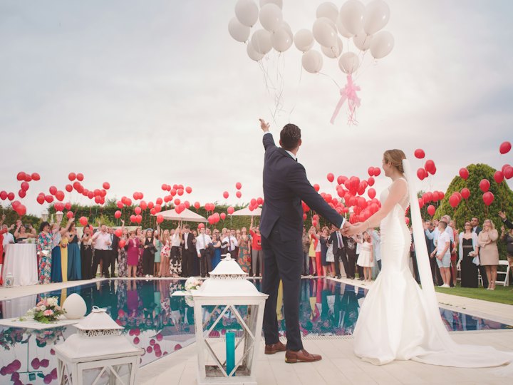 A couple and their guests releasing red balloons by the water
